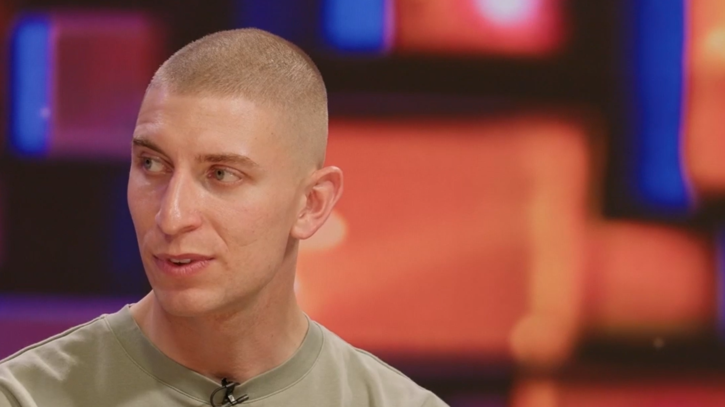 Jacob Darkin, sitting a the Reframed desk. They have a shaved head and are wearing a khaki tshirt.