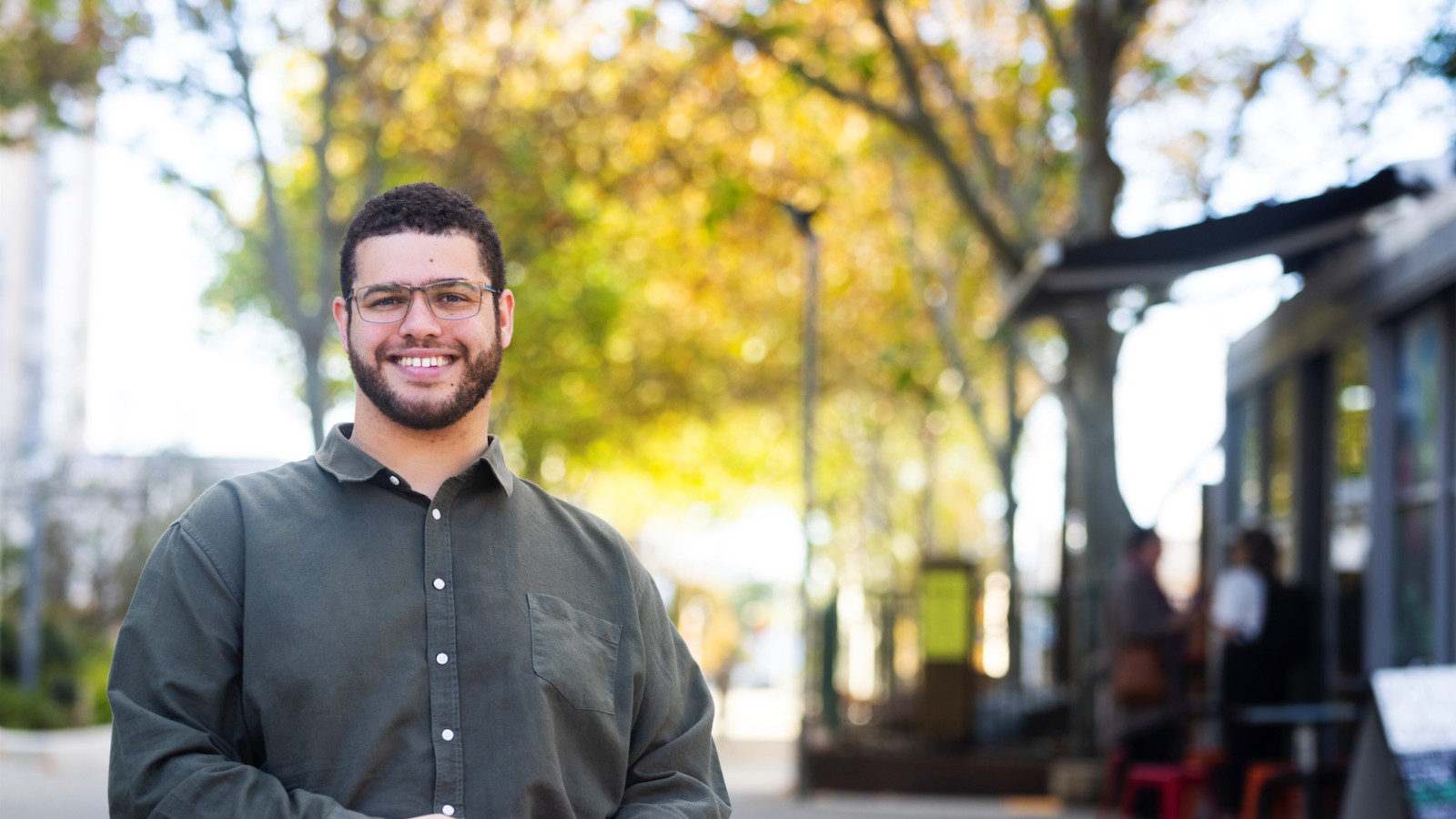 Jordon Steele-John in a dark shirt and white pants sits smiling at the camera