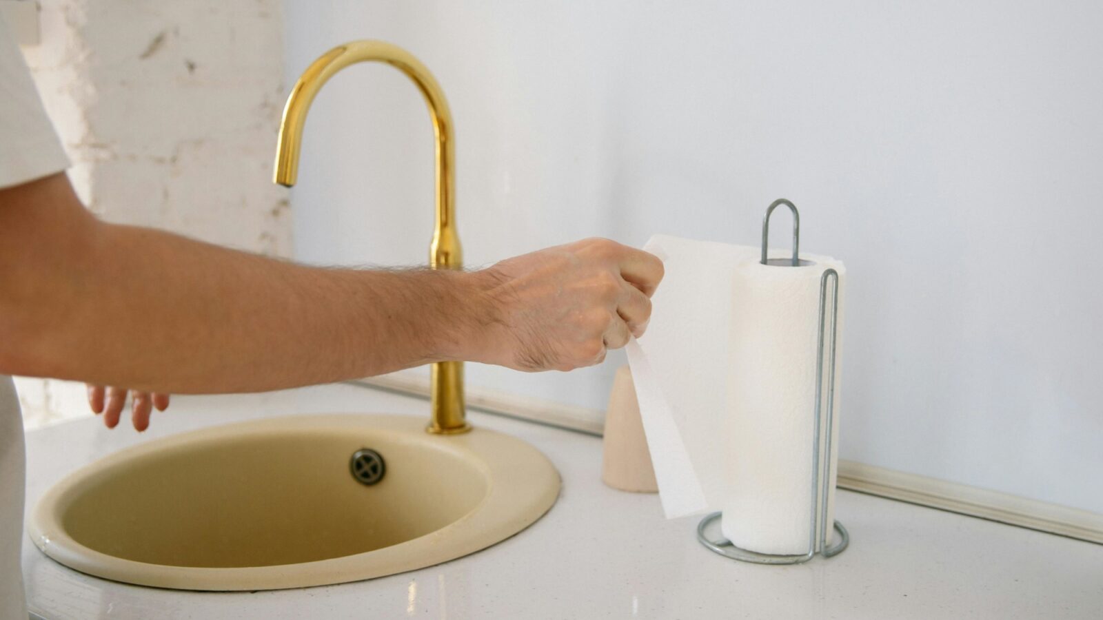 A person puling a paper towel off a holder at a bathroom sink