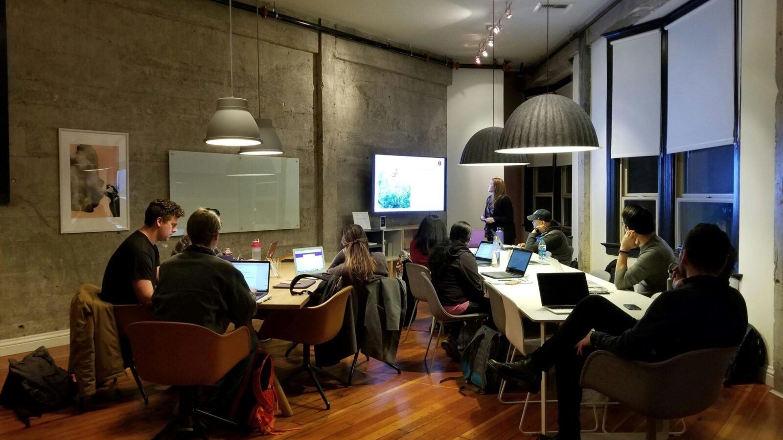 An open plan work area with people at a few different tables, working on laptops