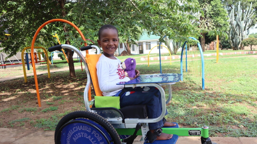 a photo of a young Tanzanian girl in a blue, green, and orange wheelchair