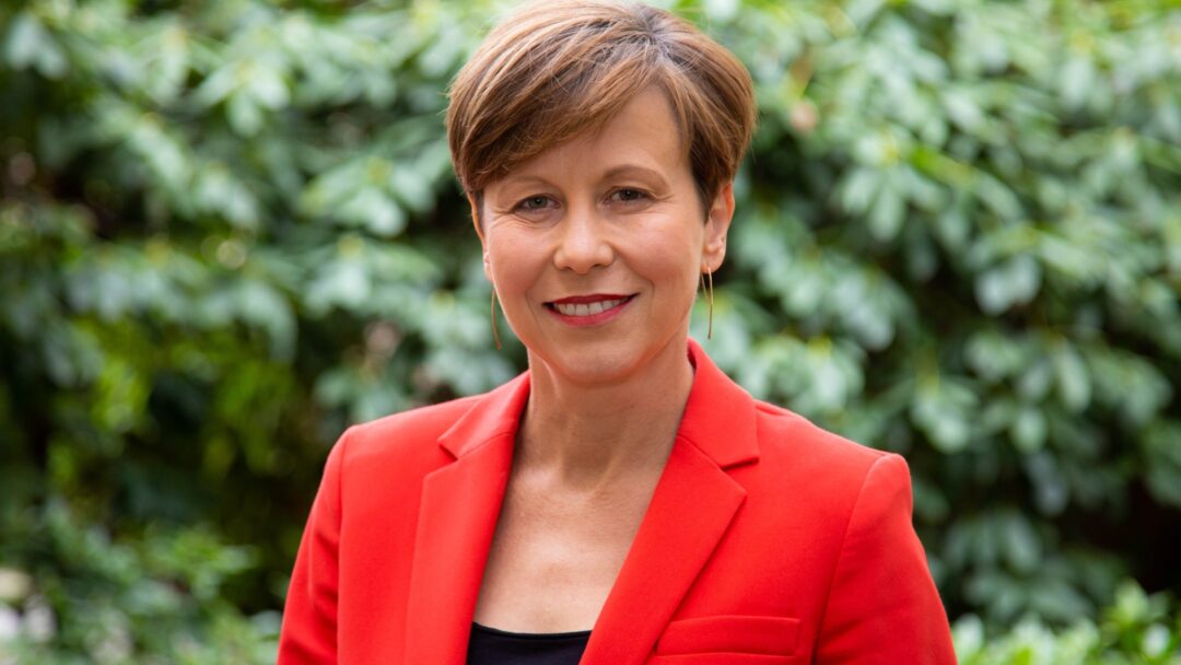 Jenny McAllister Minister for NDIS a smiling woman in a red jacket and black shirt.