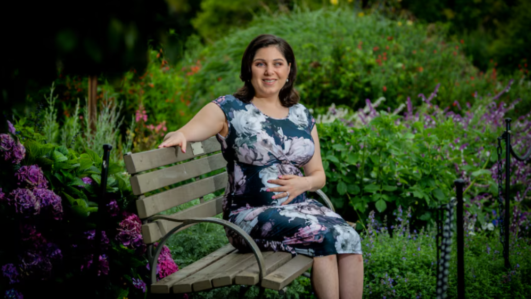 Nas sitting on a garden bench. She is wearing a floral dress and surrounded by greenery.