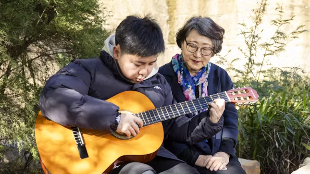 An older woman watches a child play acoustic guitar