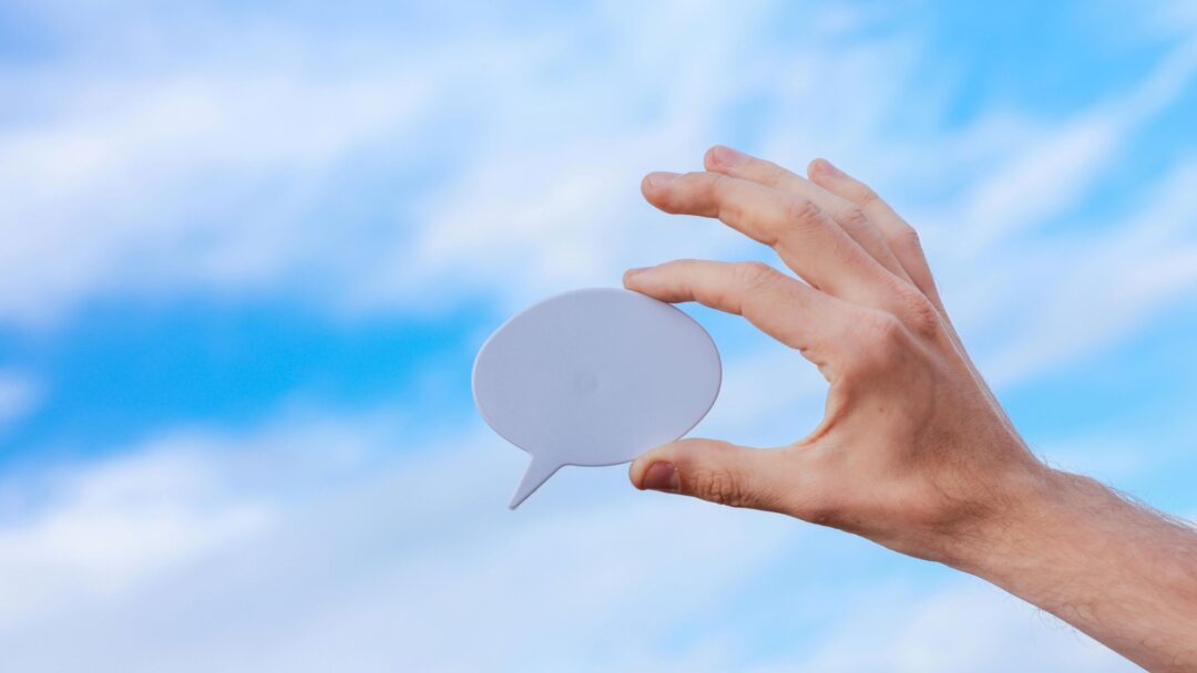 A hand holding a speech bubble against a blue sky
