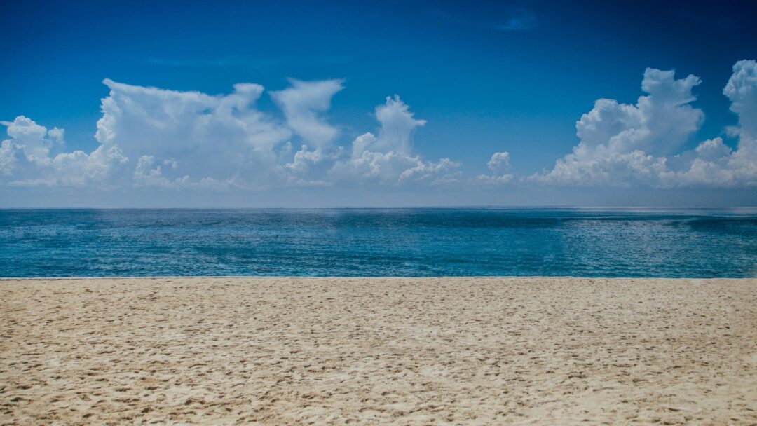 A photo of a sandy beach with blue water and a cloudy sky