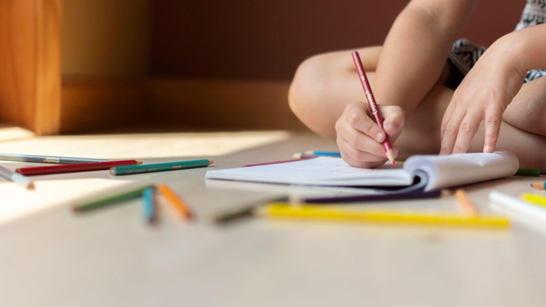 A child sitting on the floor holding a pencil over a notebook