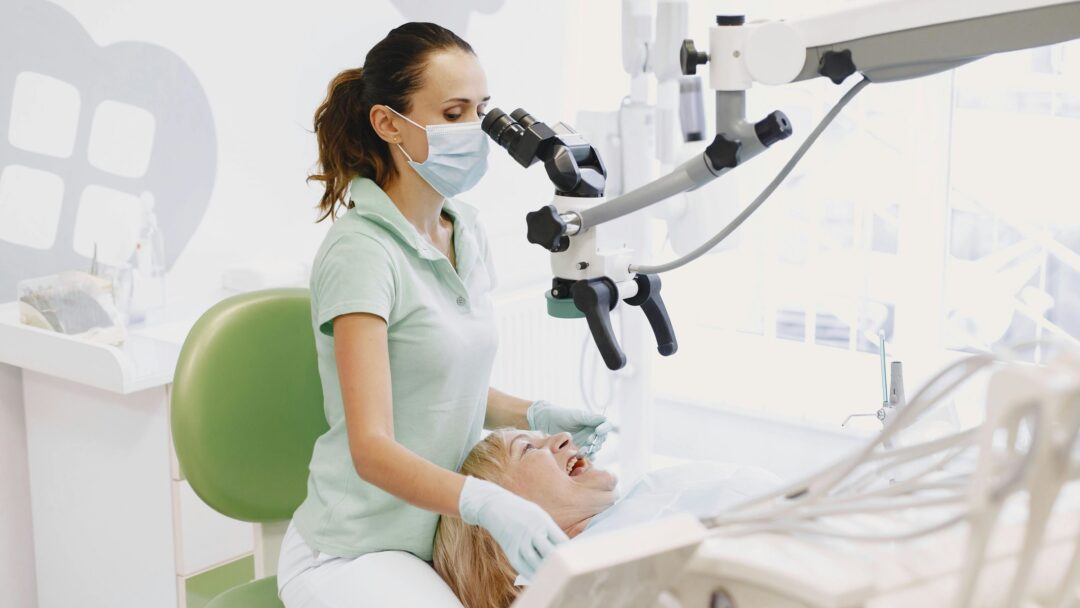 A dentist in a surgical mask looking through tools at a patient who has their mouth open