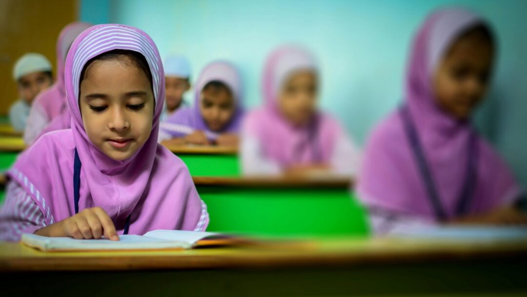 Children sitting at a row of desks reading books
