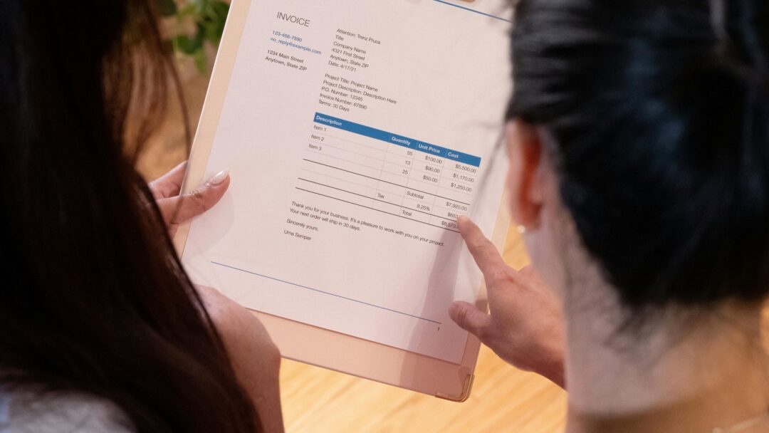 A photo showing the backs of two peoples heads looking at an invoice on a clipboard