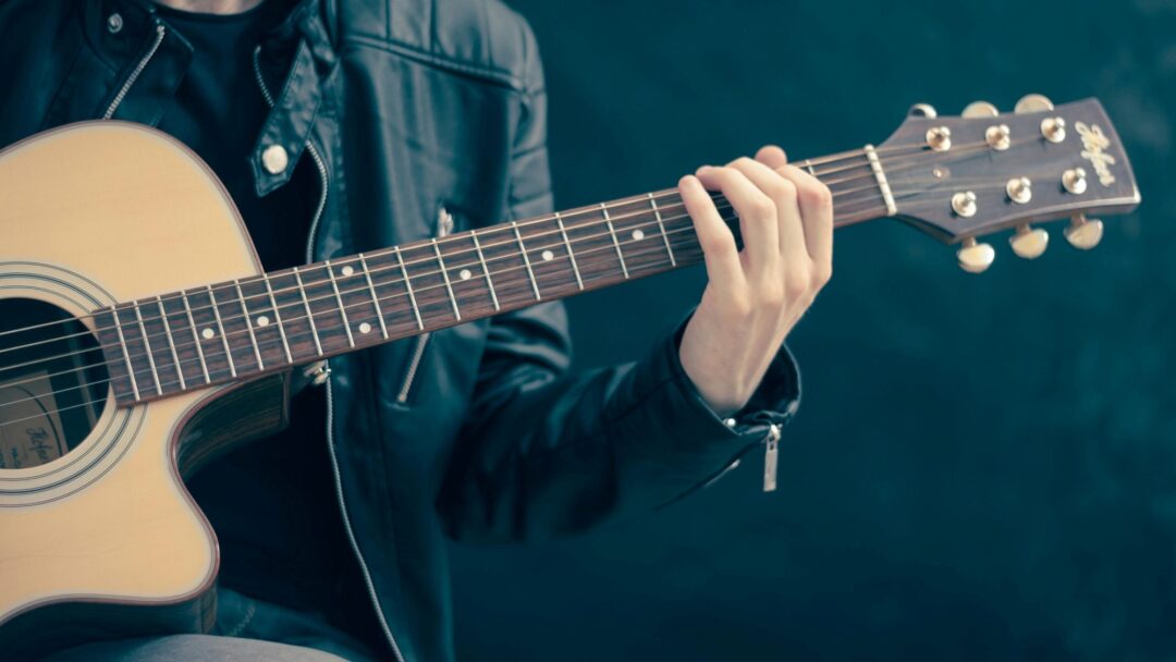 A person holding a six string acoustic guitar with a single cut out.