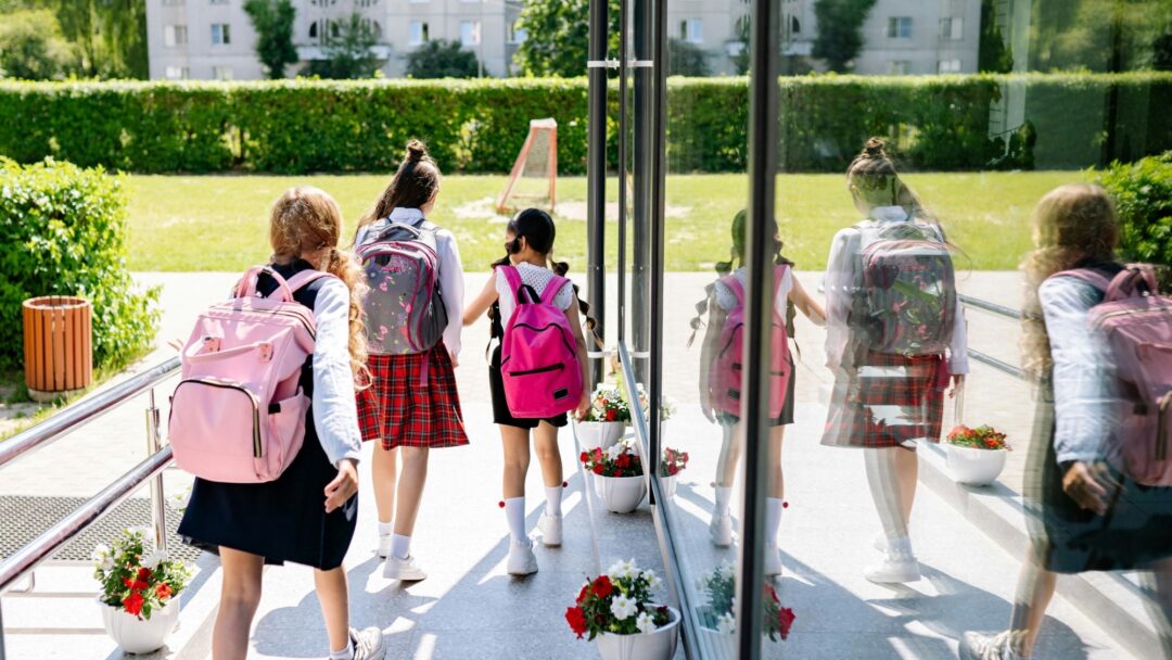 Three children wearing backpacks leaving a classroom