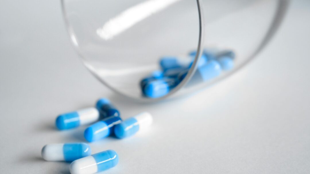 Blue and white tablets falling from a clear glass