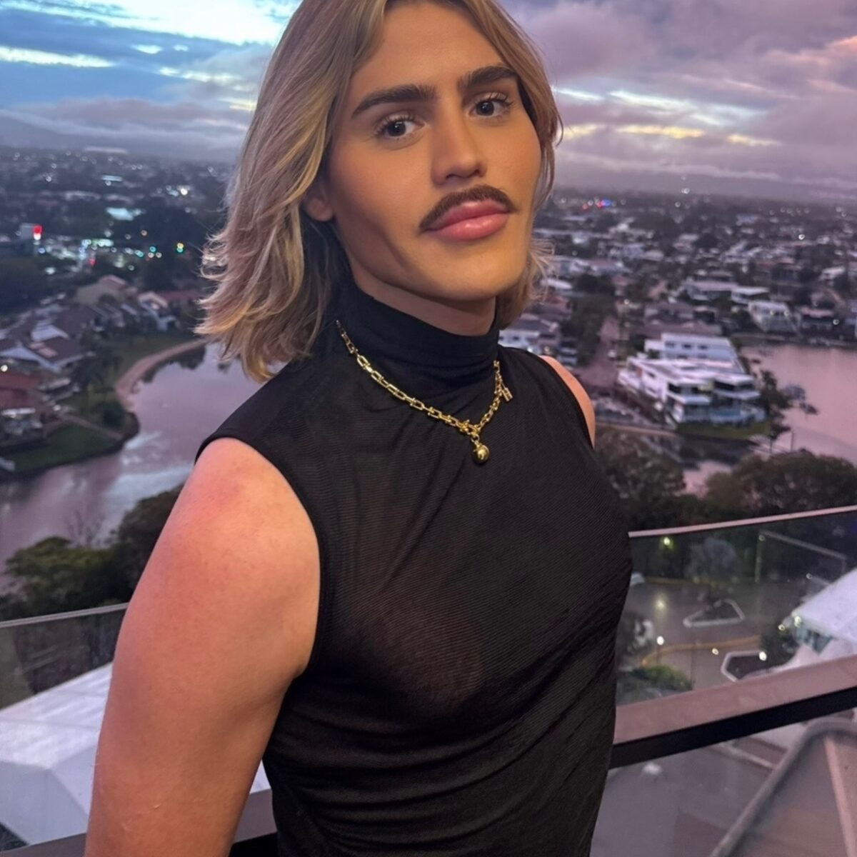 Patrick Rory John, a psychotherapist, on a high balcony wearing a black top and necklace.