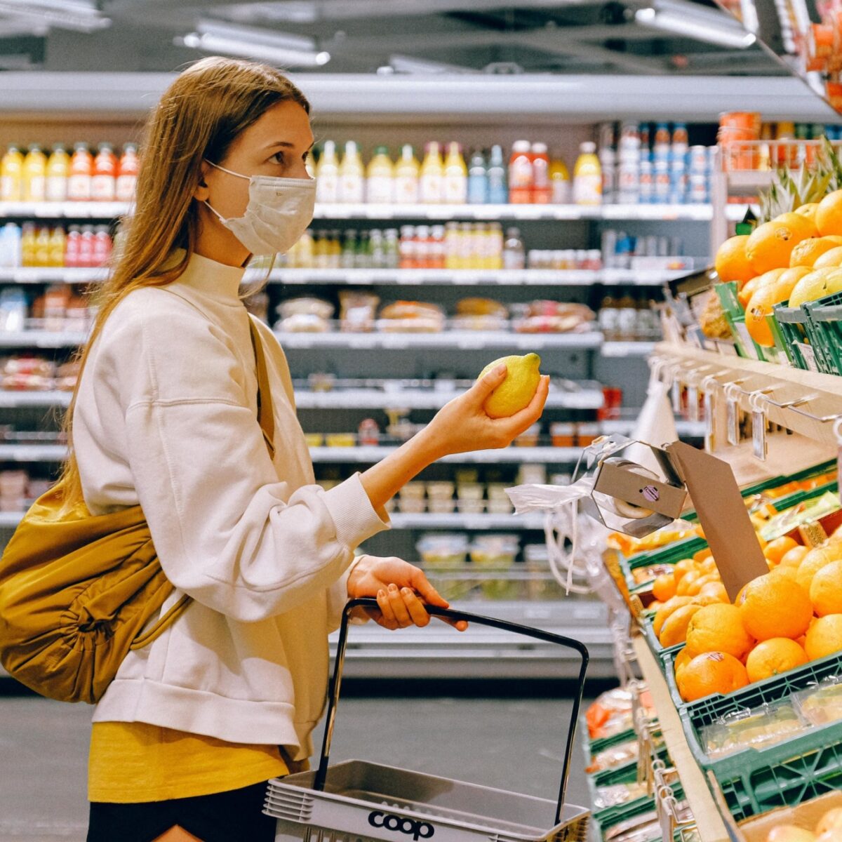 A person in a surgical mask holds fruit in a grocery store