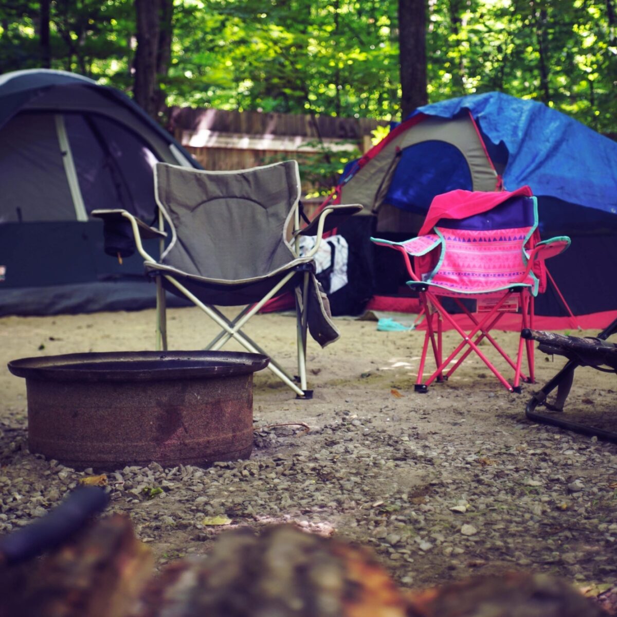 Two small tents and two camping chairs around an empty fire pit.