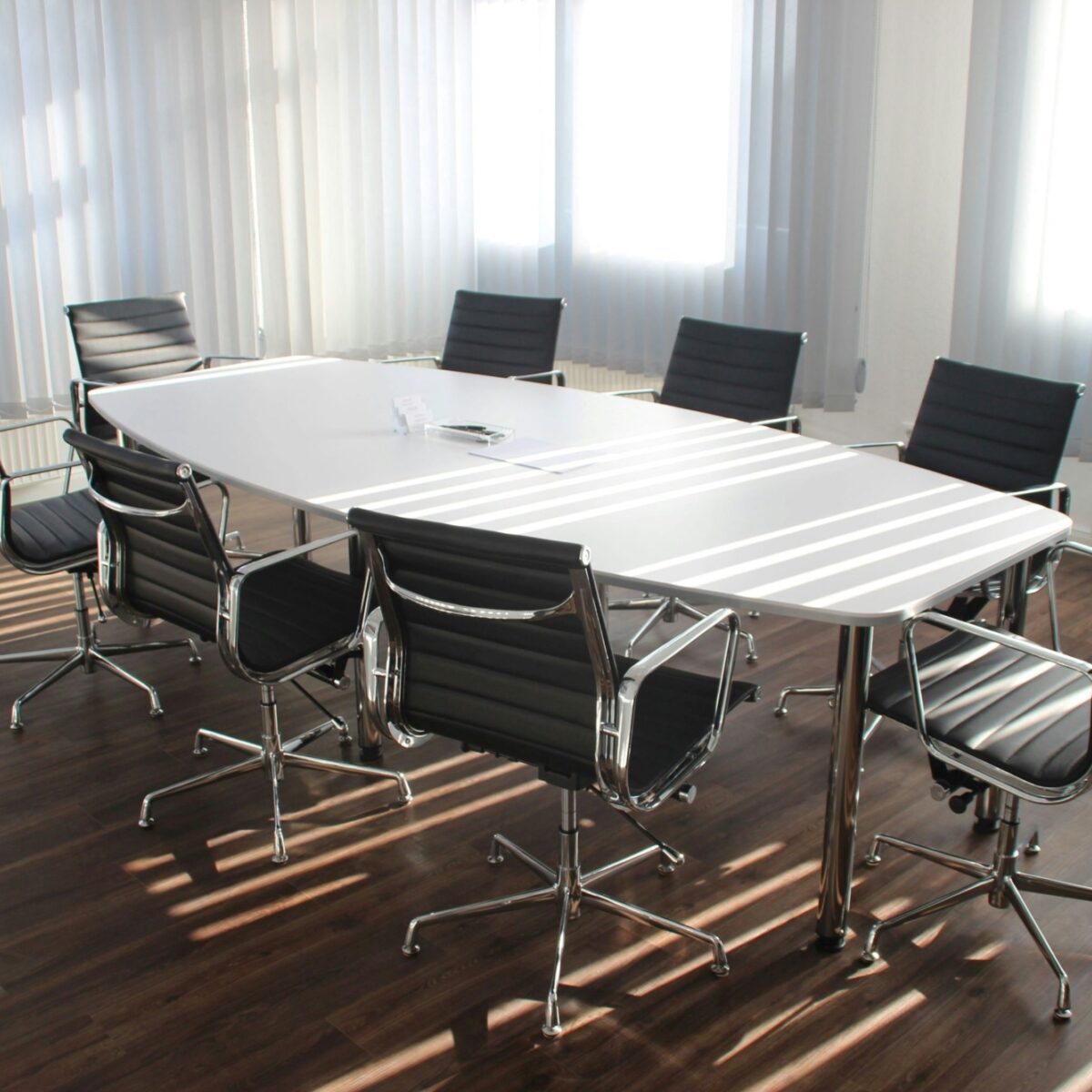 An empty meeting room with a white table and eight black chairs