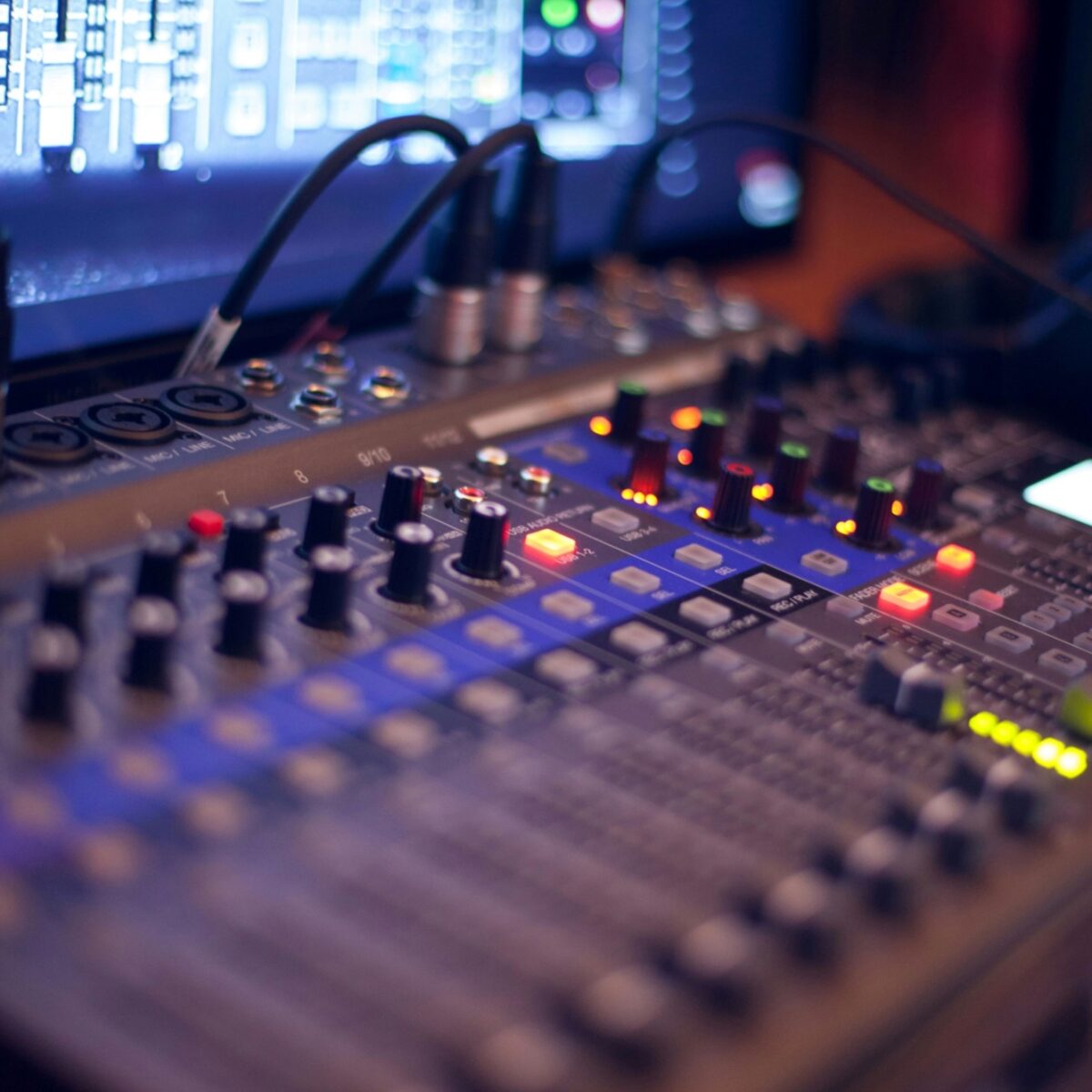 An audio mixing console in front of a computer screen