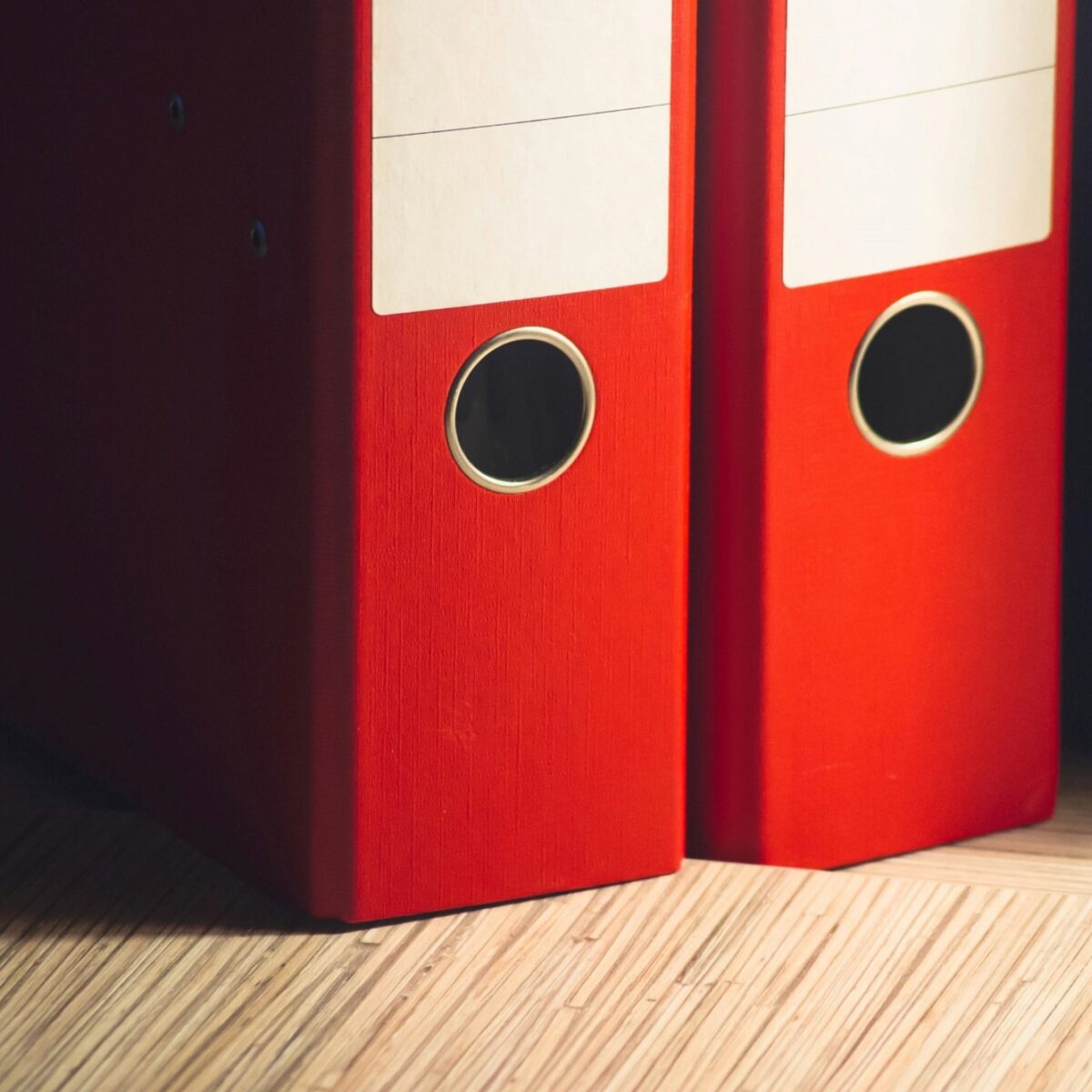 Two red binders sitting on a fake wood shelf.