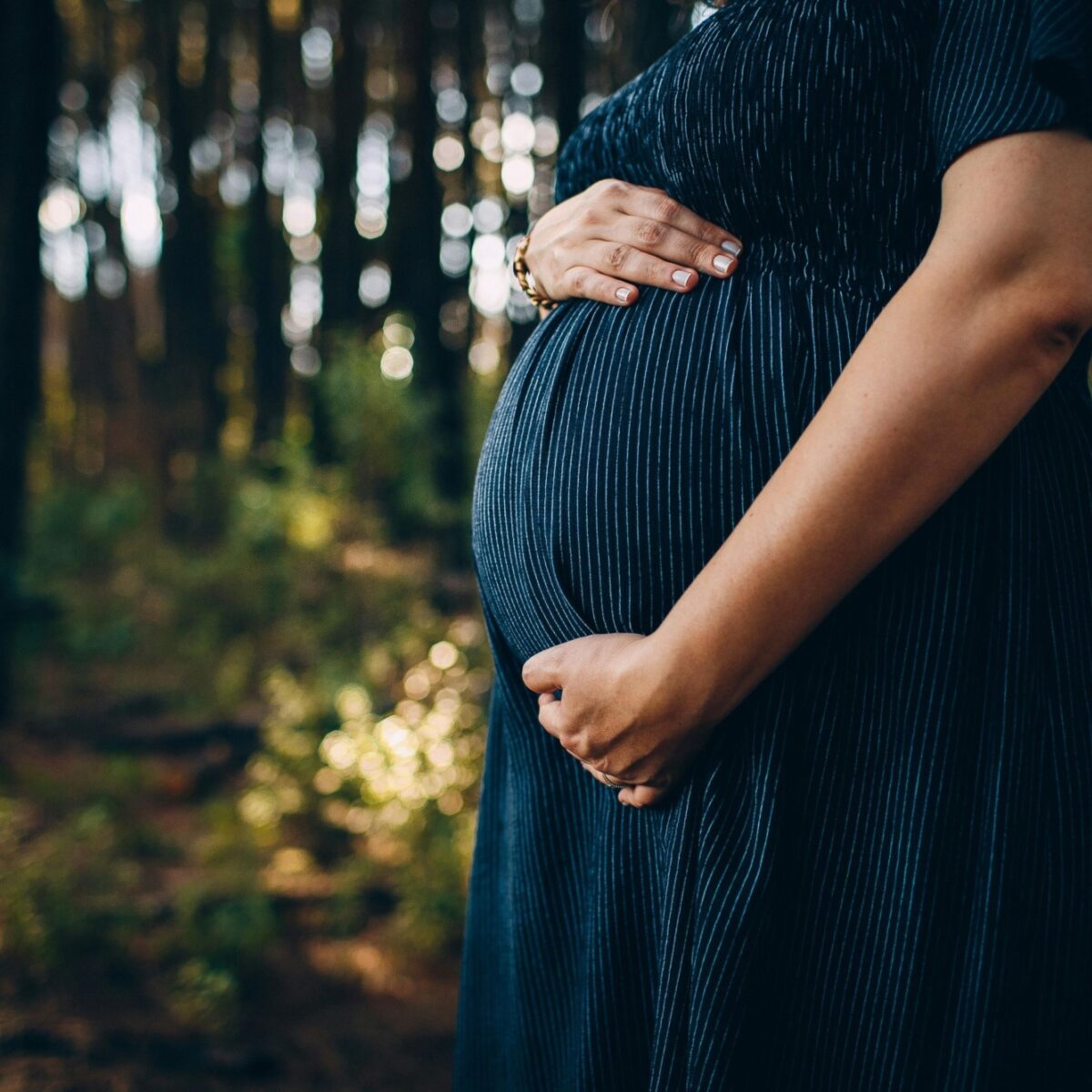 A pregnant person holding their stomach in a forest