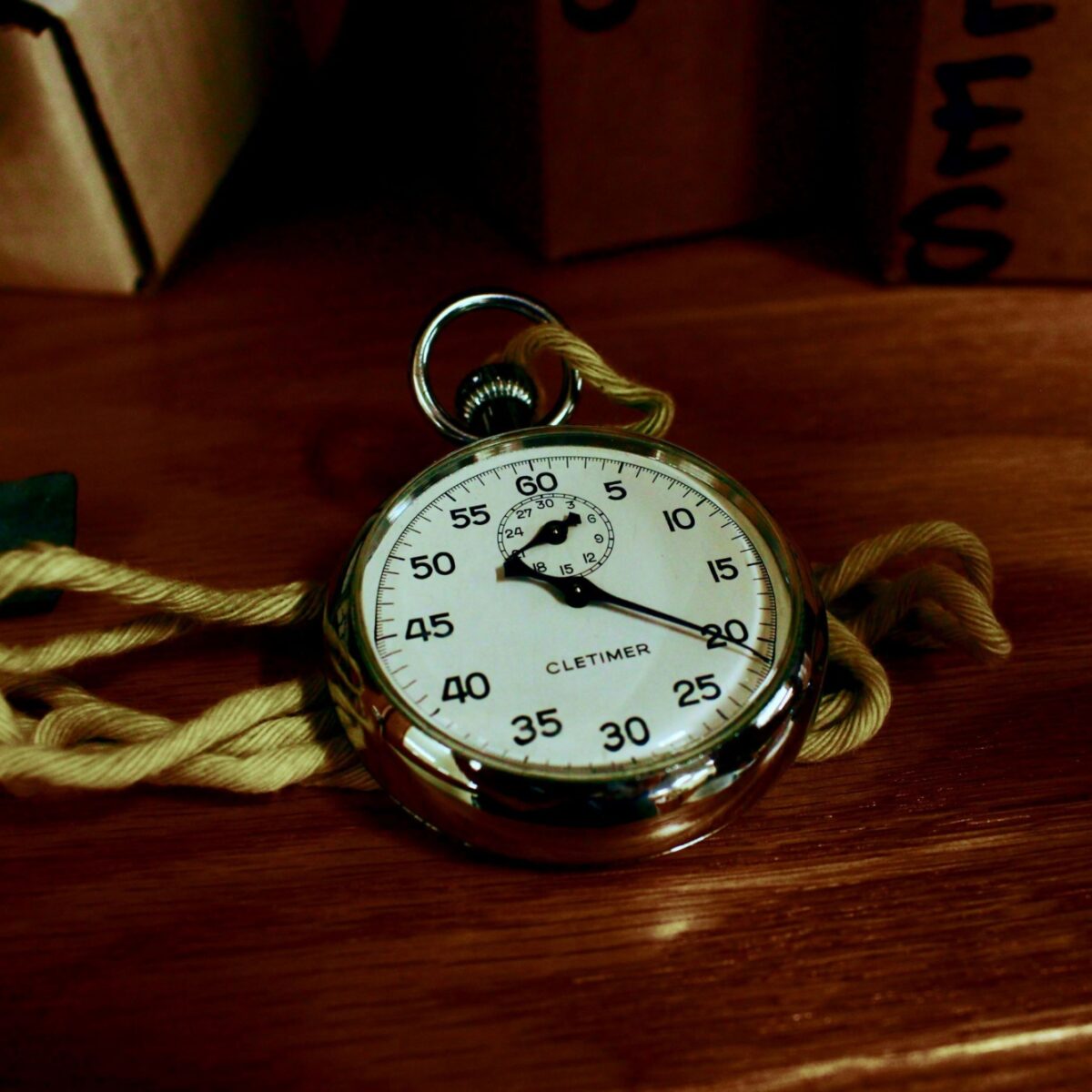 A metal or chrome framed stopwatch is resting on a dark wooden table.